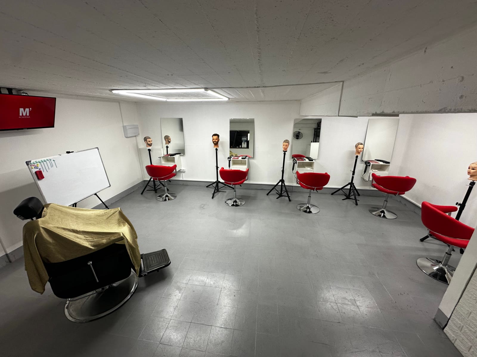 Salón de práctica de la Academia del Barbero: estaciones con espejos, sillas rojas y cabezas de práctica